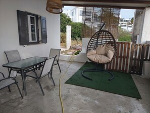 Um pátio com mesa de vidro, cadeiras, uma cadeira suspensa e um tapete verde.