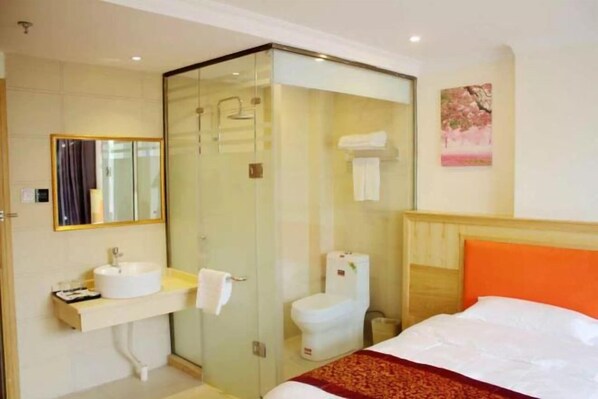 A hotel room with a glass-enclosed shower, a white sink, a toilet, and a bed with an orange headboard. - Changyue Hotel (Beihai High-speed Railway Station) (Beihai)