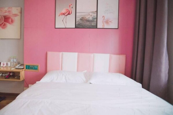 A hotel room with a pink wall, a bed with white bedding, a nightstand with a phone, and a painting of flamingos. - Changyue Hotel (Beihai High-speed Railway Station) (Beihai)
