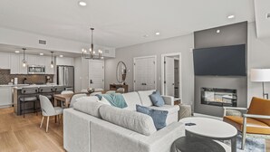 A modern living room with a grey sofa, a dining area, a kitchen, and a fireplace. - New Top Floor 3Bed/2Bath, sleeps 8. Outdoor pool and Hot Tub Open Year Round! (Dead Man's Flats)