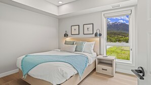 A modern bedroom with a large bed, bedside tables, a window with a mountain view, and framed artwork on the wall. - New Top Floor 3Bed/2Bath, sleeps 8. Outdoor pool and Hot Tub Open Year Round! (Dead Man's Flats)