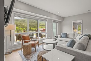 Ein modernes Wohnzimmer mit großem Fenster, einer Couch, einem runden Couchtisch und einem Sessel.