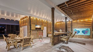 Un intérieur rustique avec des meubles en bois, des tables et des chaises, un mur en bois orné d’un tableau et une grande colonne en bois.