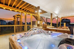 A wooden outdoor hot tub area with a view of the city at sunset. - Sleeps 20, 4 King BR, Beach Access, Luxury Spa, Decks, Pets, Games Galore (Bolivar Peninsula)