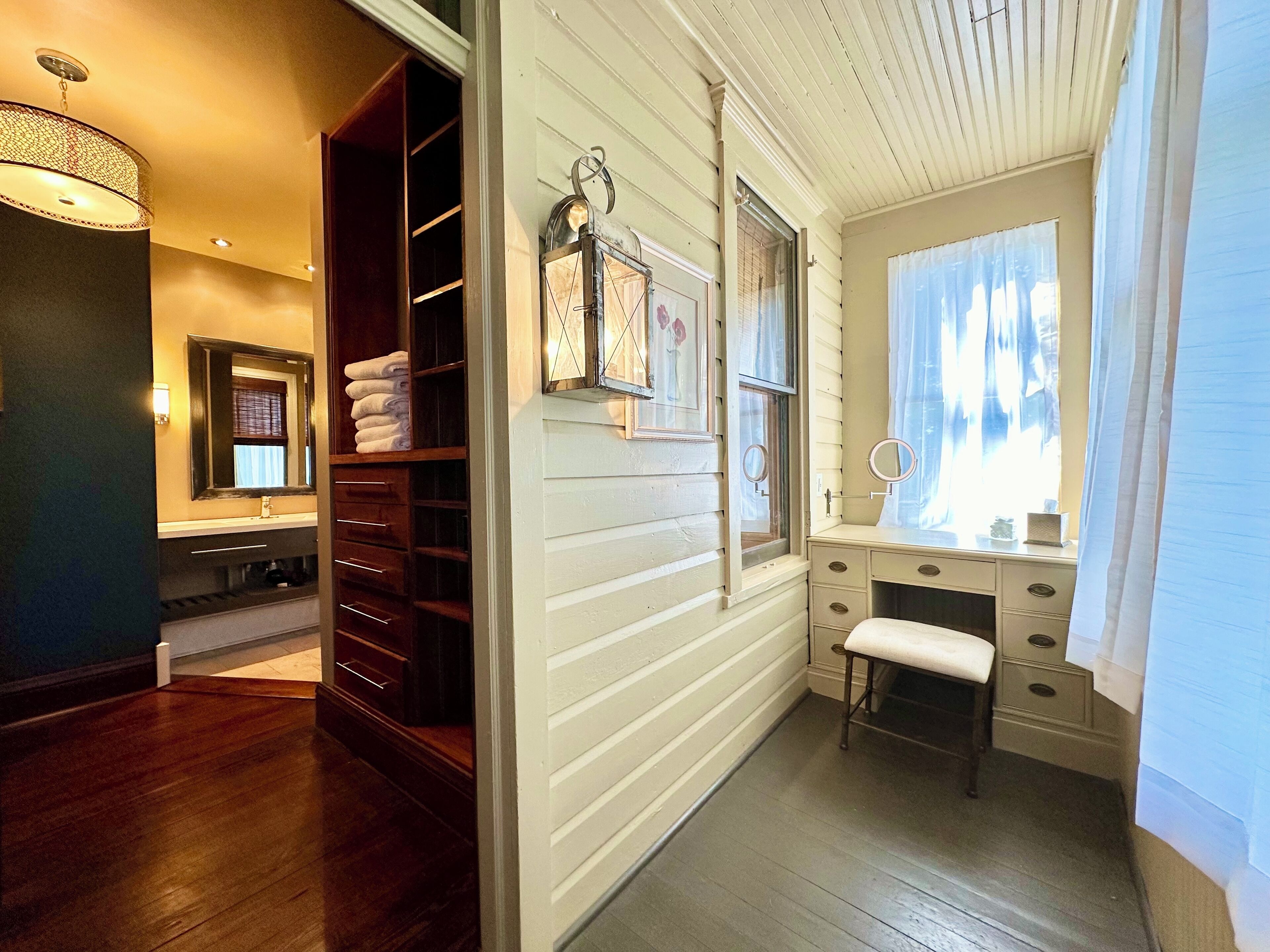 Une salle de bain avec un meuble-lavabo, un miroir, une fenêtre avec des rideaux et un plancher en bois.