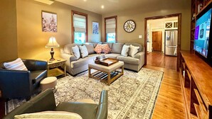 A living room with a sofa, coffee table, and a TV. There is a clock on the wall and a window with blinds. - 2,200 Sq Ft w/ 2 Gamerooms, Firepit & Grill 15 Minutes To Hershey (Palmyra)