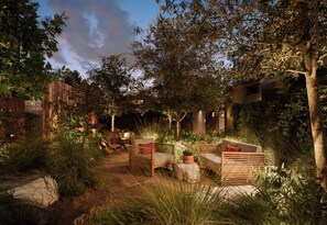 An outdoor seating area with wooden furniture and a potted plant, surrounded by trees and greenery.