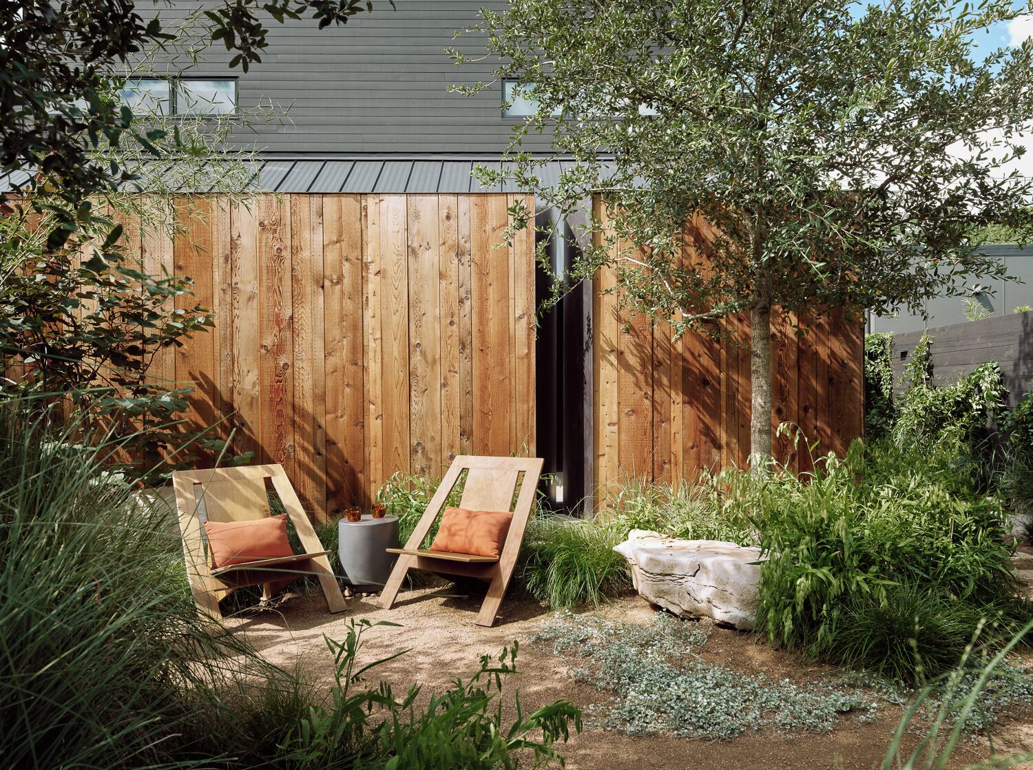 A wooden fence, two wooden chairs, a small potted plant, and a rock in a garden area.