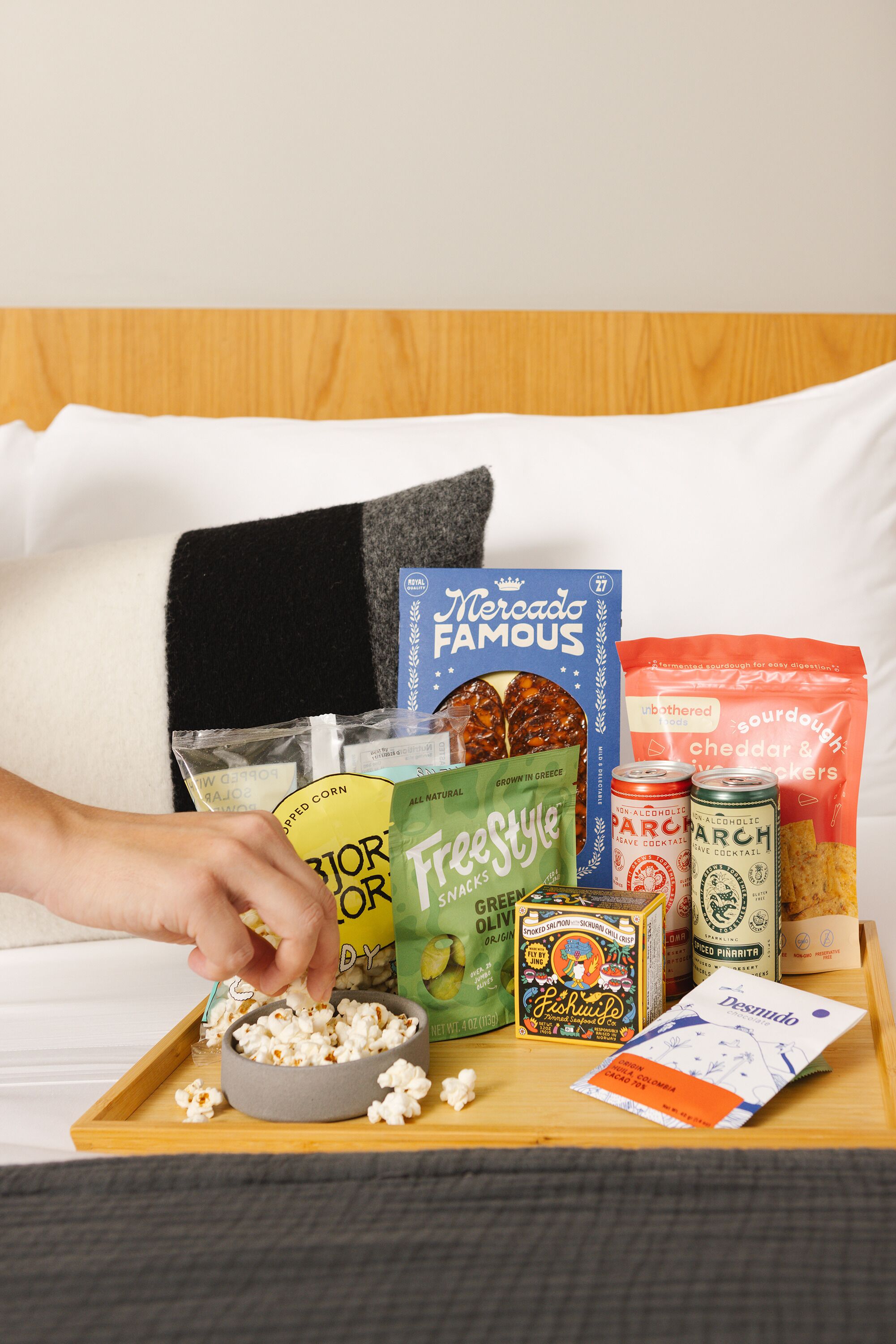 A tray with popcorn, snacks, and drinks on a bed.