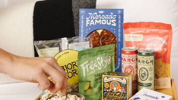 A tray with popcorn, snacks, and drinks on a bed.