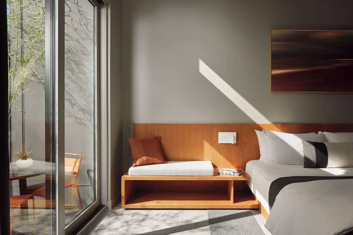 A modern bedroom with a wooden headboard, a bedside table, and a large window.