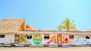 Un edificio con tejado de paja, un mural publicitando desayuno, almuerzo y cena, y un letrero dando la bienvenida a los huéspedes.