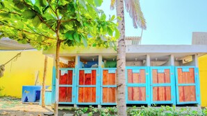 Un edificio con varias habitaciones, algunas con puertas azules y otras con puertas rojas, y un árbol en la parte delantera.