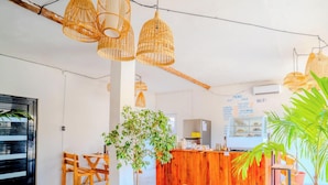 Una cafetería con muebles de madera, lámparas colgantes de mimbre y una pizarra con el menú.