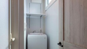 A narrow bathroom with a white sink, a mirror, and a white appliance, likely a washing machine or dryer. - Sakura (Nagoya)