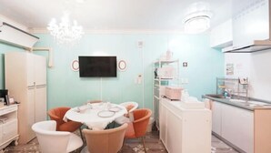 A compact kitchen with a dining area, a flat-screen TV mounted on the wall, and a small refrigerator. - Sakura (Nagoya)