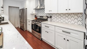 A modern kitchen with white cabinets, stainless steel appliances, and a marble countertop. - Cozy Gem, Hot Tub,  close to downtown Berkley shops and restaurants (Berkley)