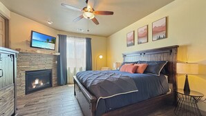 Een slaapkamer met een bed, een open haard, een plafondventilator en een aan de muur bevestigde televisie.