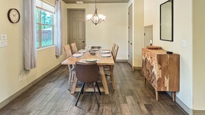 Een eetruimte met een houten tafel gedekt voor vier personen, een kroonluchter en een houten kast met lades.