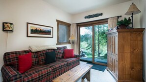 Una sala de estar acogedora con un sofá a cuadros, un banco de madera, un armario de madera y un ventanal con vistas a zonas verdes.
