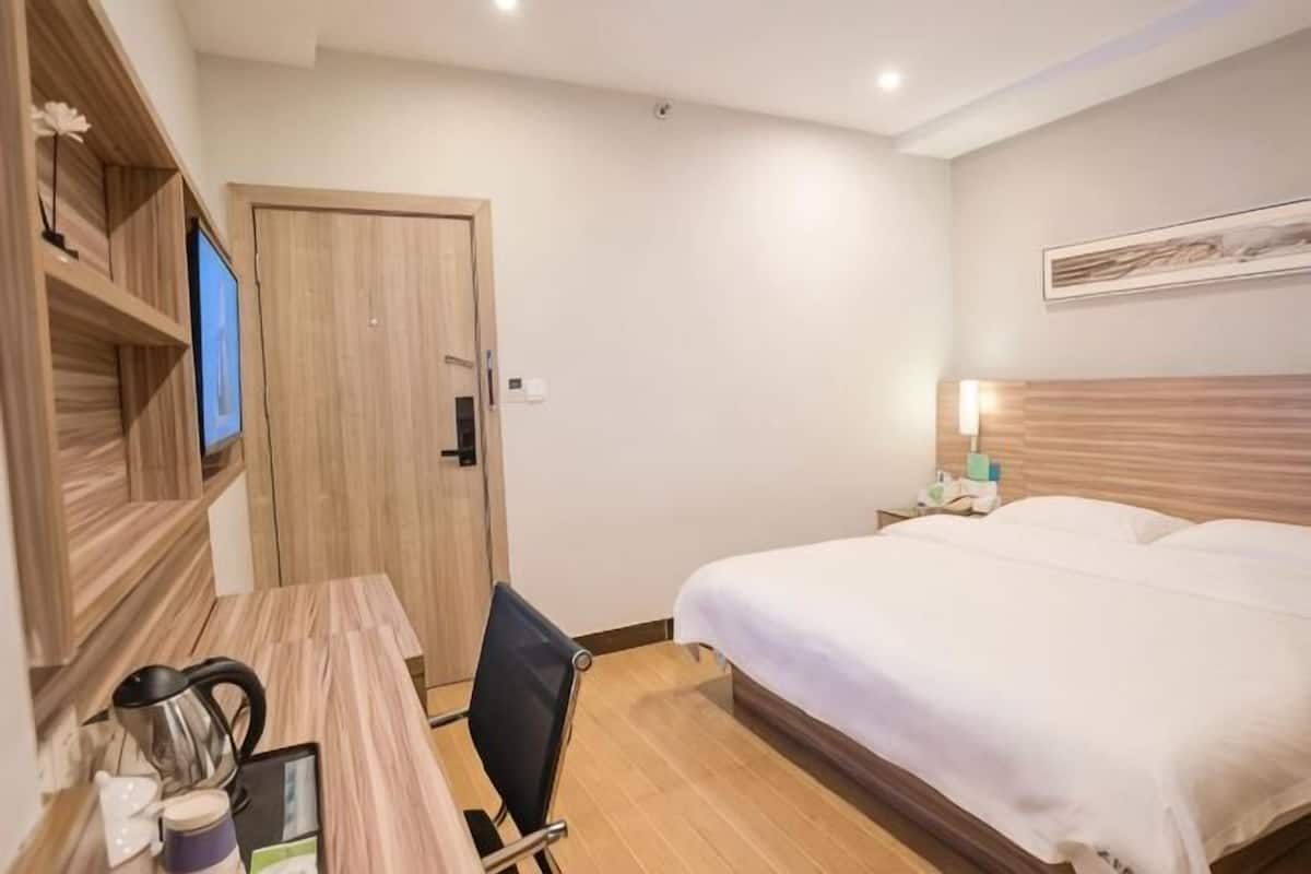 A hotel room with a bed, a desk with a chair, a TV, and a wooden door.