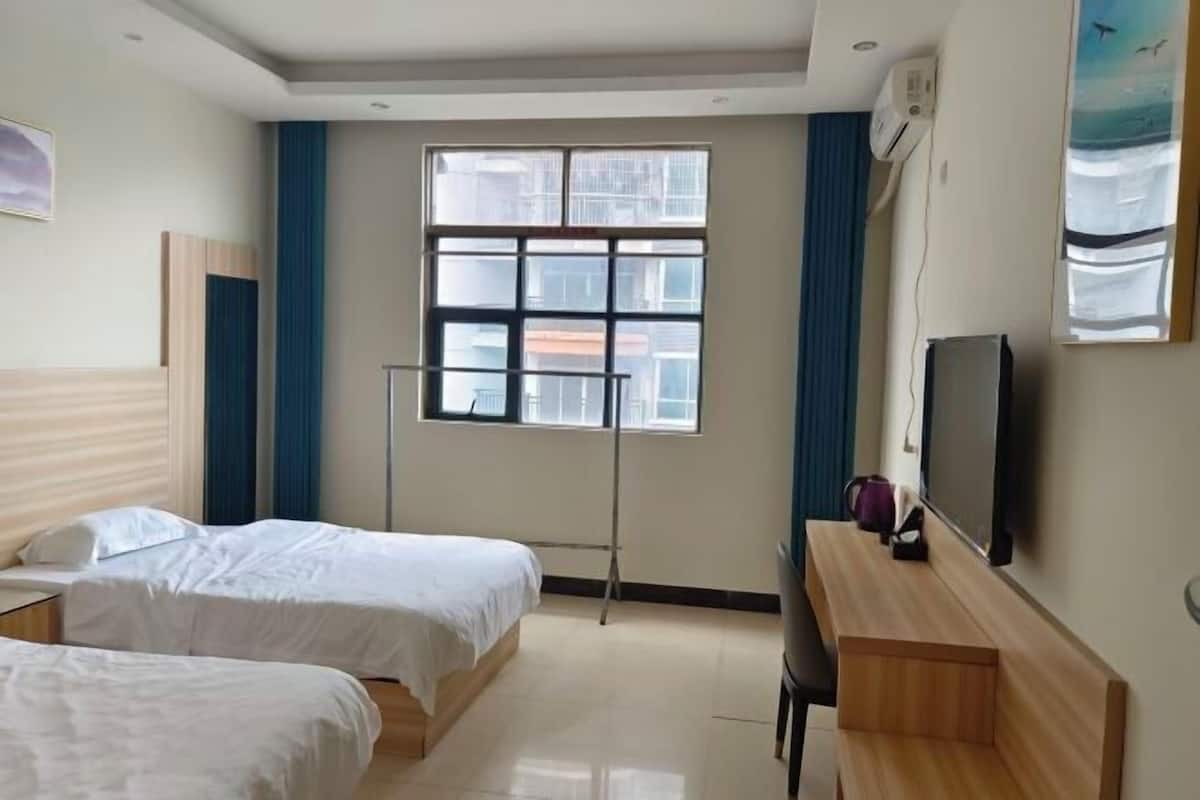 A hotel room with two beds, a desk, a TV, and a window with a view of buildings.