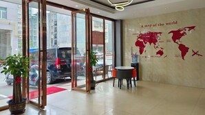 Un hall de hotel con un mapa del mundo en la pared, una puerta de vidrio de acceso y una pequeña mesa con sillas.