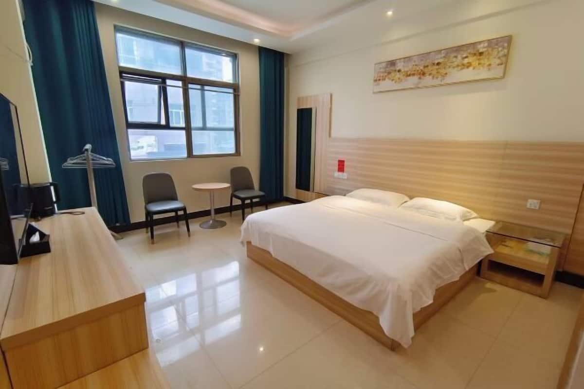 A hotel room with a bed, a desk, a chair, a small table, and a window with curtains.