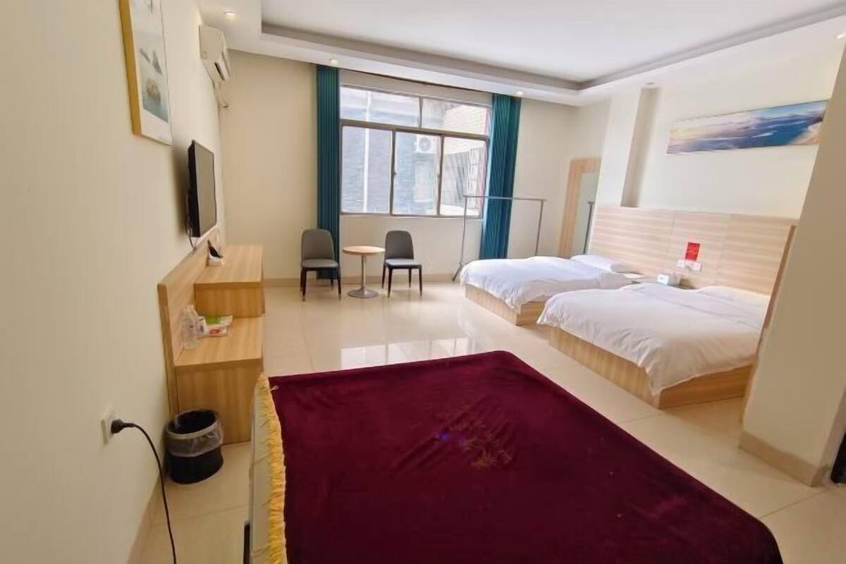A hotel room with two beds, a desk with a chair, a TV, and a window with curtains.