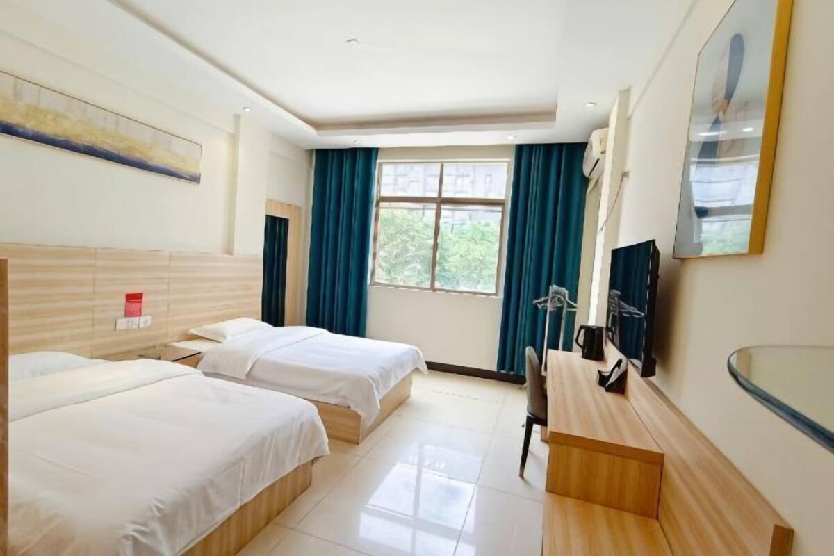 A hotel room with two beds, a desk, a chair, a TV, and a window with curtains.