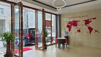 A hotel lobby with a world map on the wall, a reception desk, and a glass door entrance.