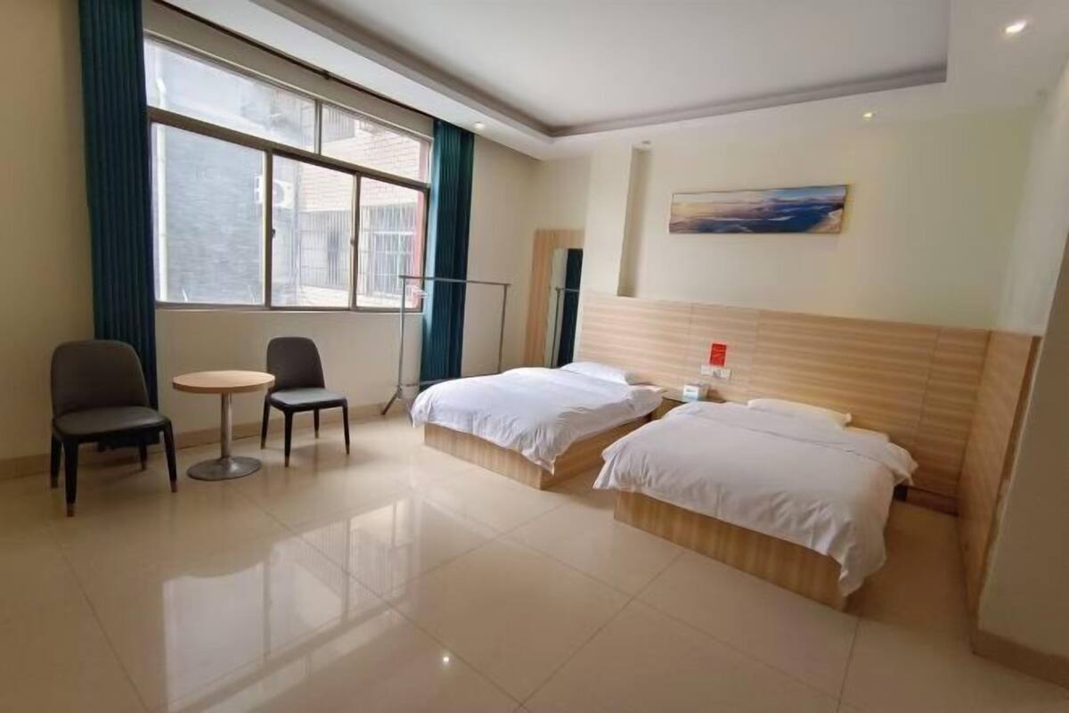A hotel room with two beds, a small round table, a chair, and a window with curtains.