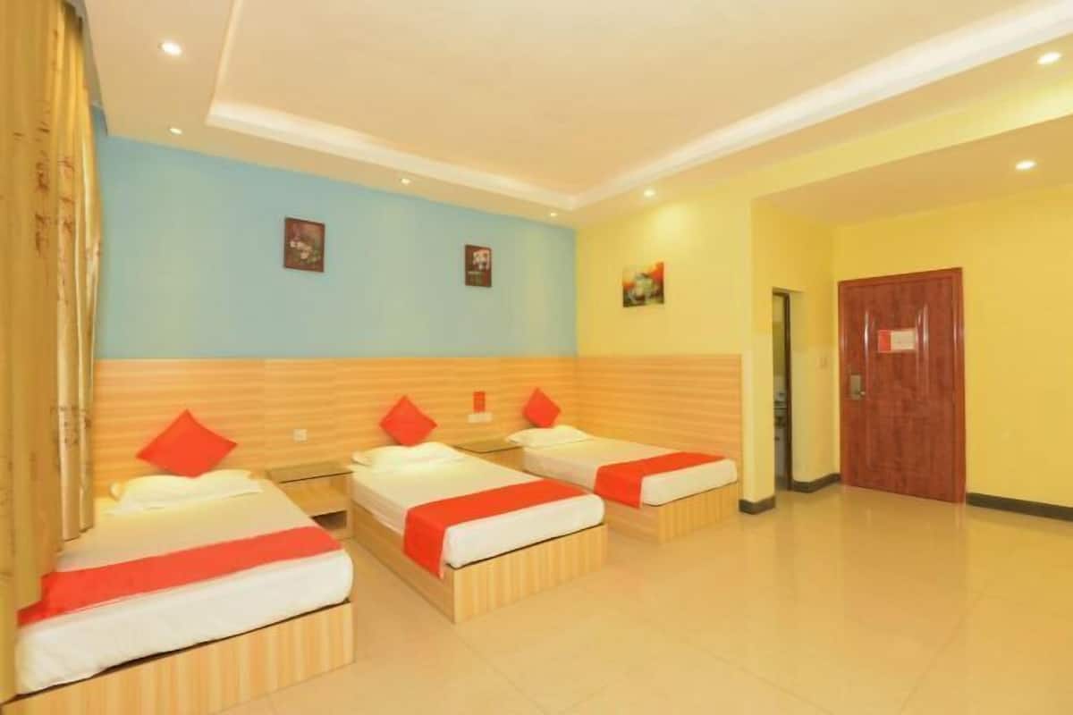 A hotel room with three beds, a wooden headboard, a blue wall, and a wooden door.