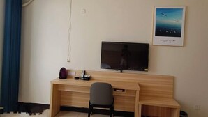 Una habitación con un escritorio de madera, una silla negra, un televisor montado en la pared y un cuadro enmarcado sobre el televisor.