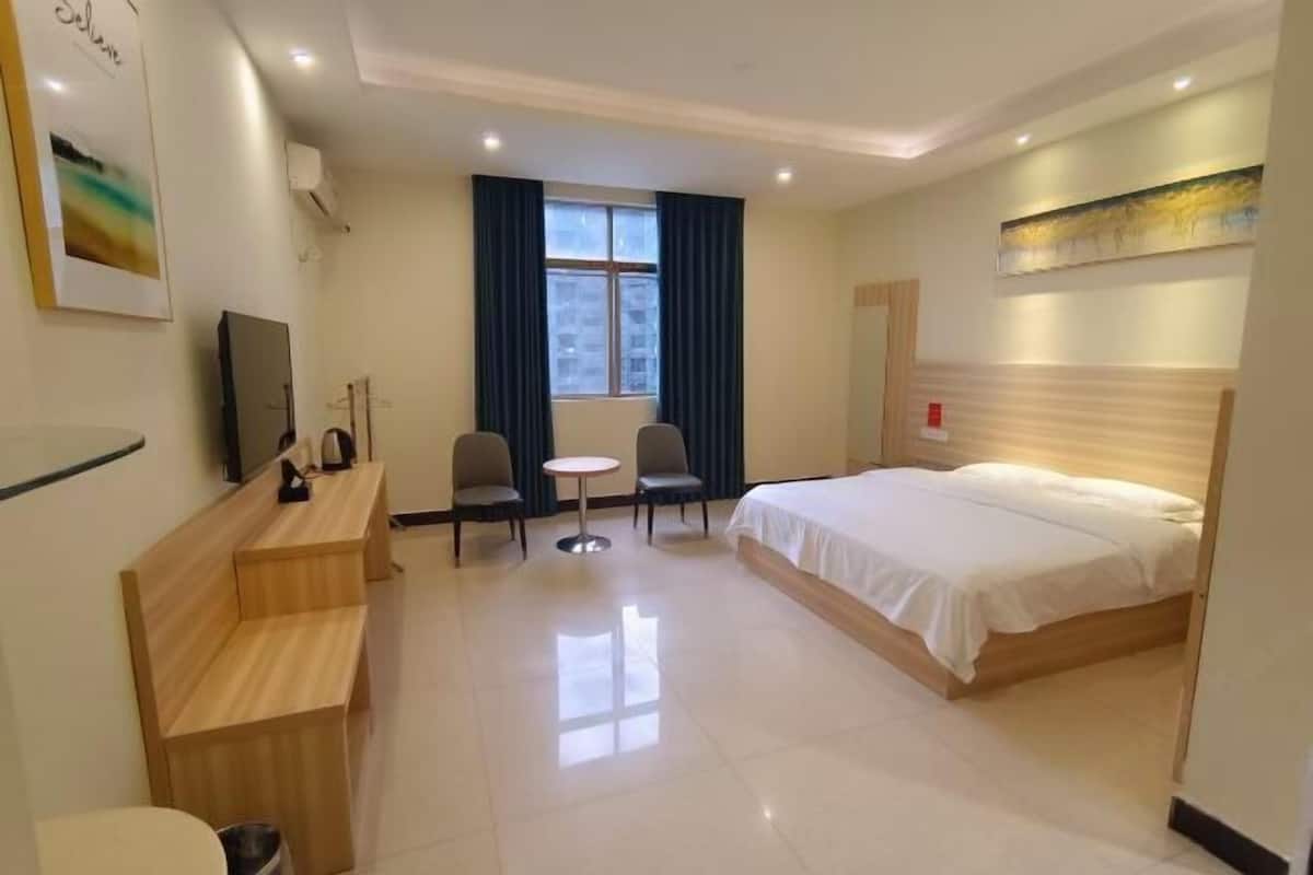 A hotel room with a bed, a desk, a chair, a small table, a TV, and a window with curtains.