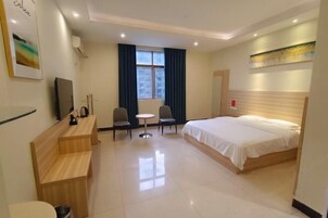 A hotel room with a bed, a desk, a chair, a small table, a TV, and a window with curtains.