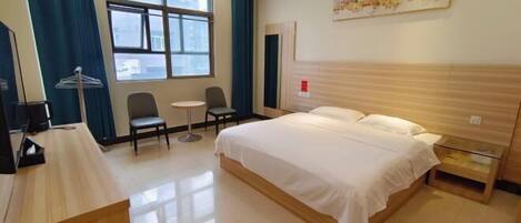 Une chambre d’hôtel avec un lit, un bureau, une chaise, une petite table et une fenêtre avec des rideaux.
