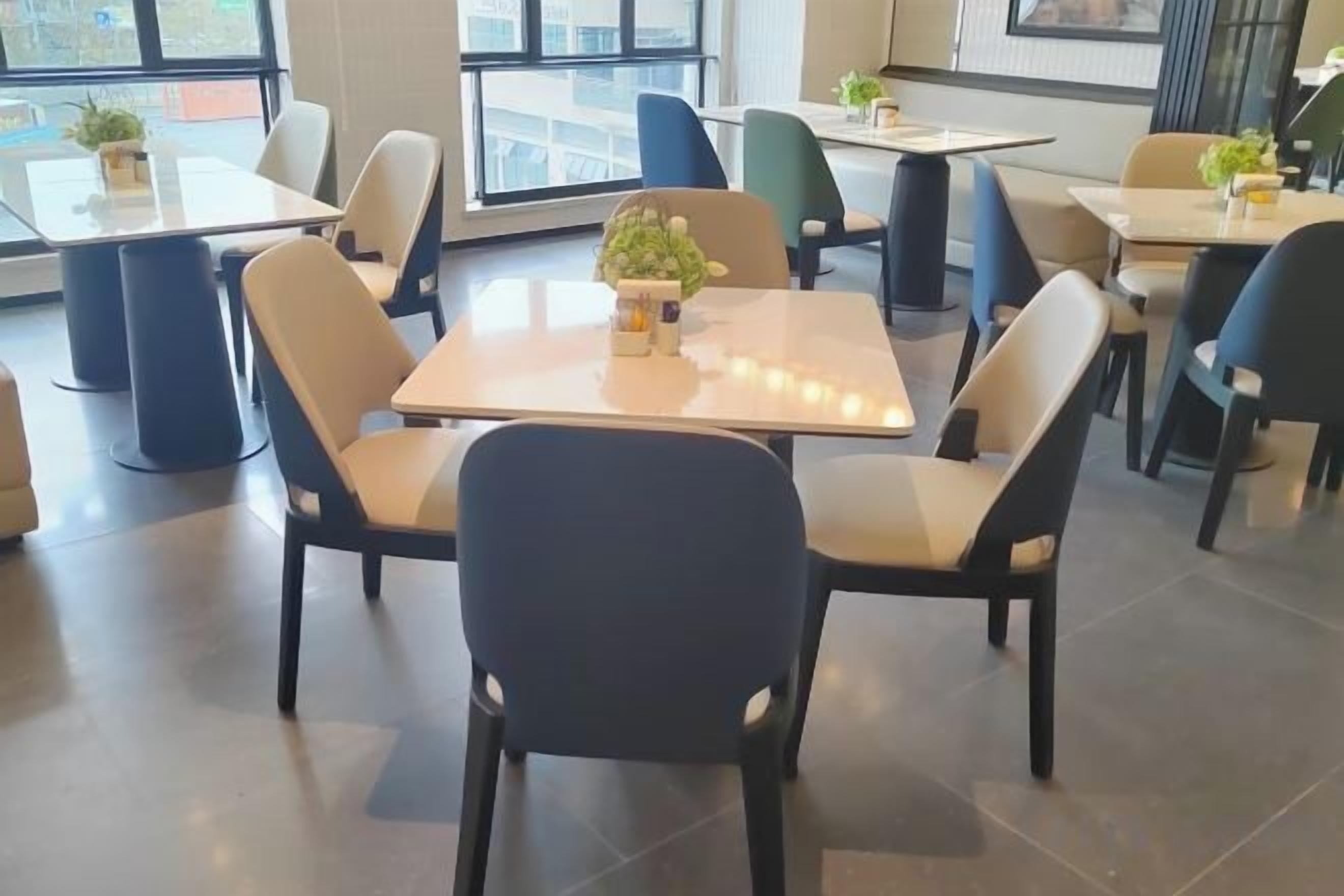 Un comedor moderno con mesas y sillas, plantas en macetas y ventanas grandes.