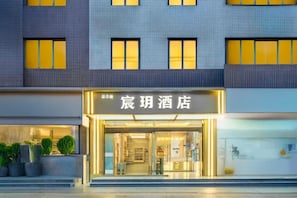 L’entrée d’un hôtel, avec une façade moderne, de grandes fenêtres et un hall d’entrée bien éclairé.