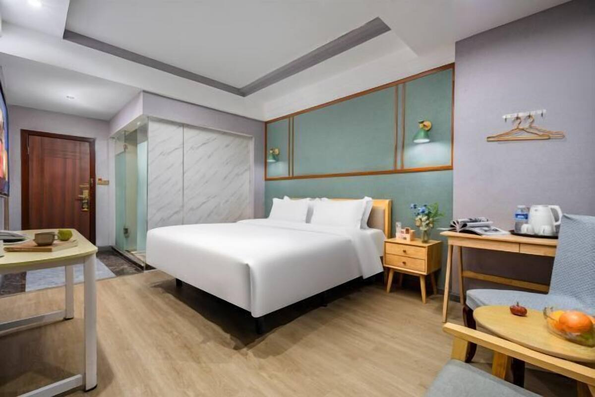 A hotel room with a bed, a desk, a chair, a wardrobe, and a small table with a bowl of fruit.