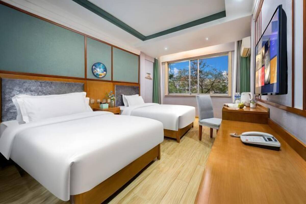 A hotel room with two beds, a desk with a telephone, and a window with a view.