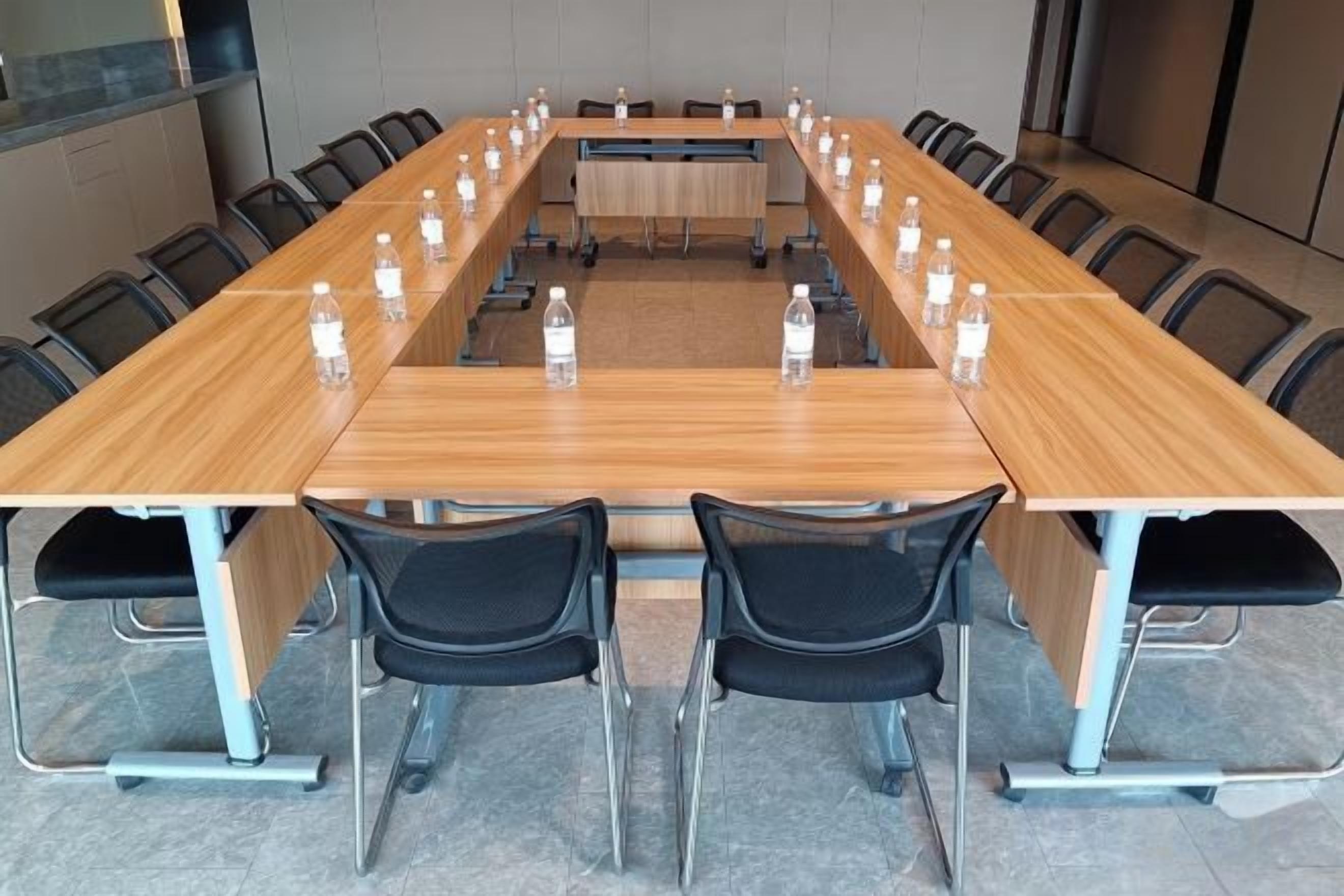 Un salón de conferencias con una mesa larga, sillas y botellas de agua.
