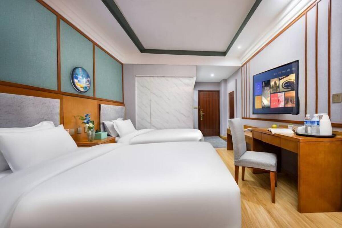 A hotel room with two beds, a desk, a chair, a television, and a door.