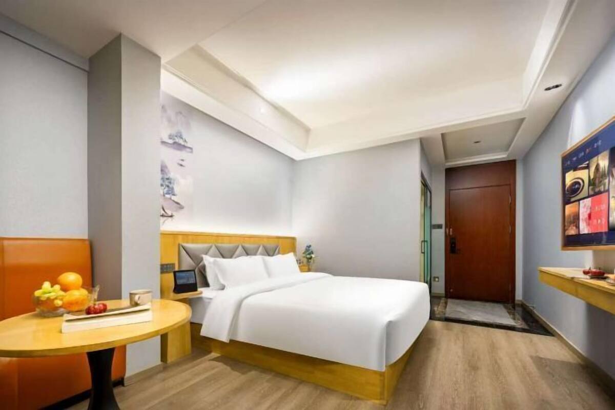 A hotel room with a bed, bedside table, and a small table with fruit.