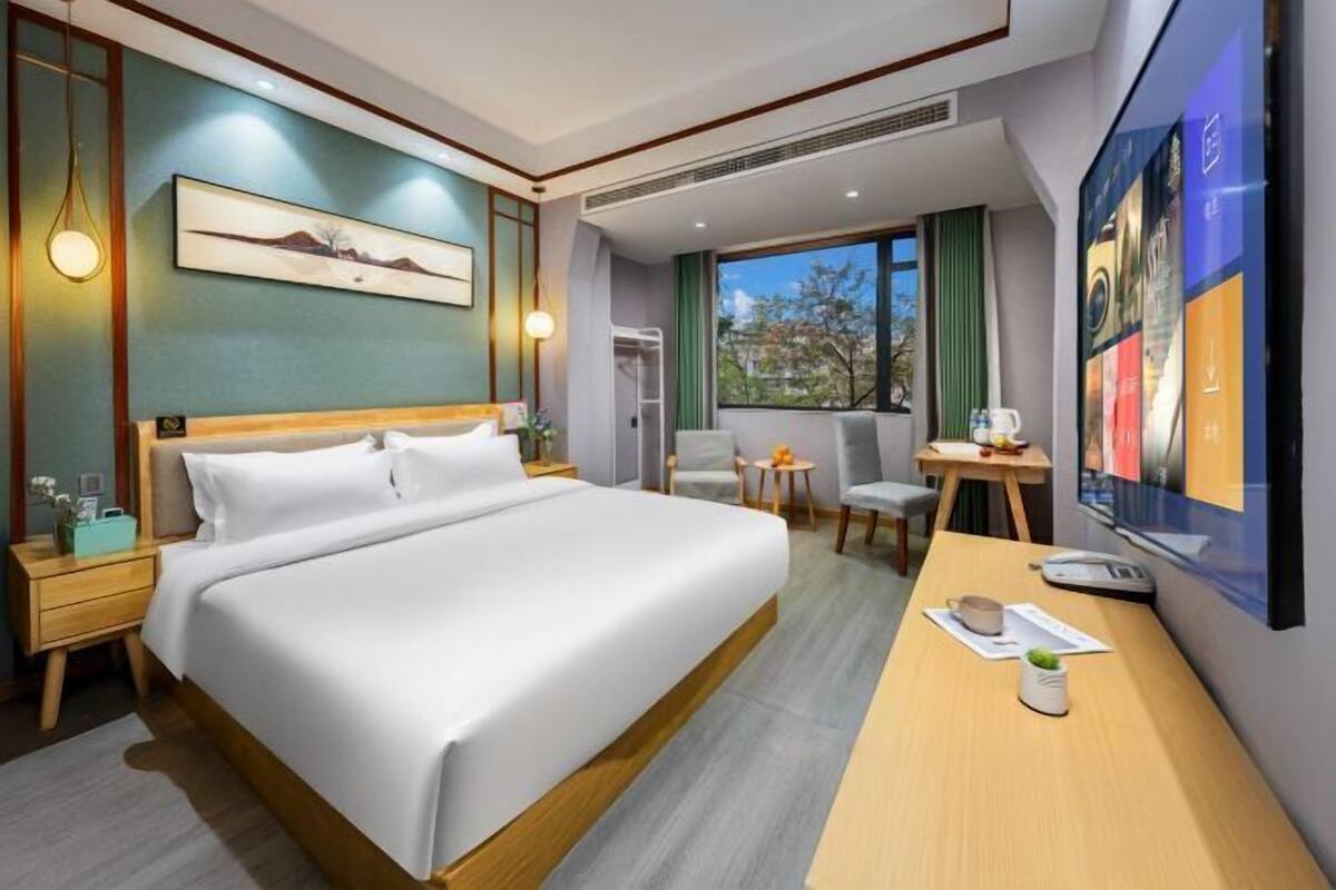 A hotel room with a large bed, a desk, a chair, a TV, and a window with a view.