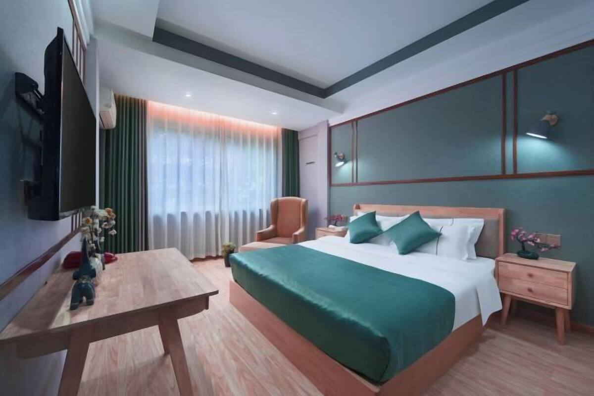 A hotel room with a bed, bedside tables, a desk, a chair, a TV, and a window with curtains.