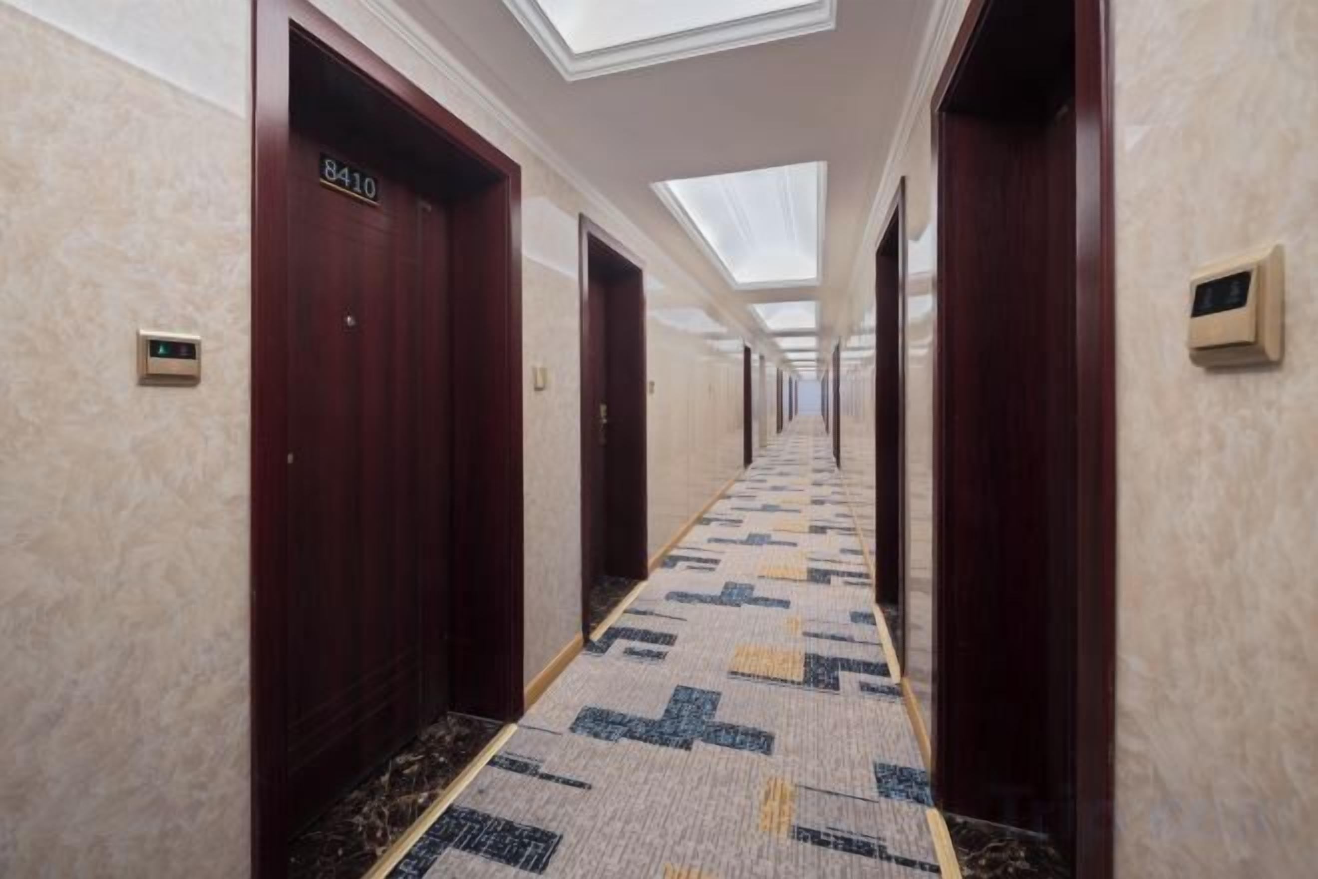 Un pasillo de hotel con puertas de madera, placas con números de habitación y una alfombra estampada.
