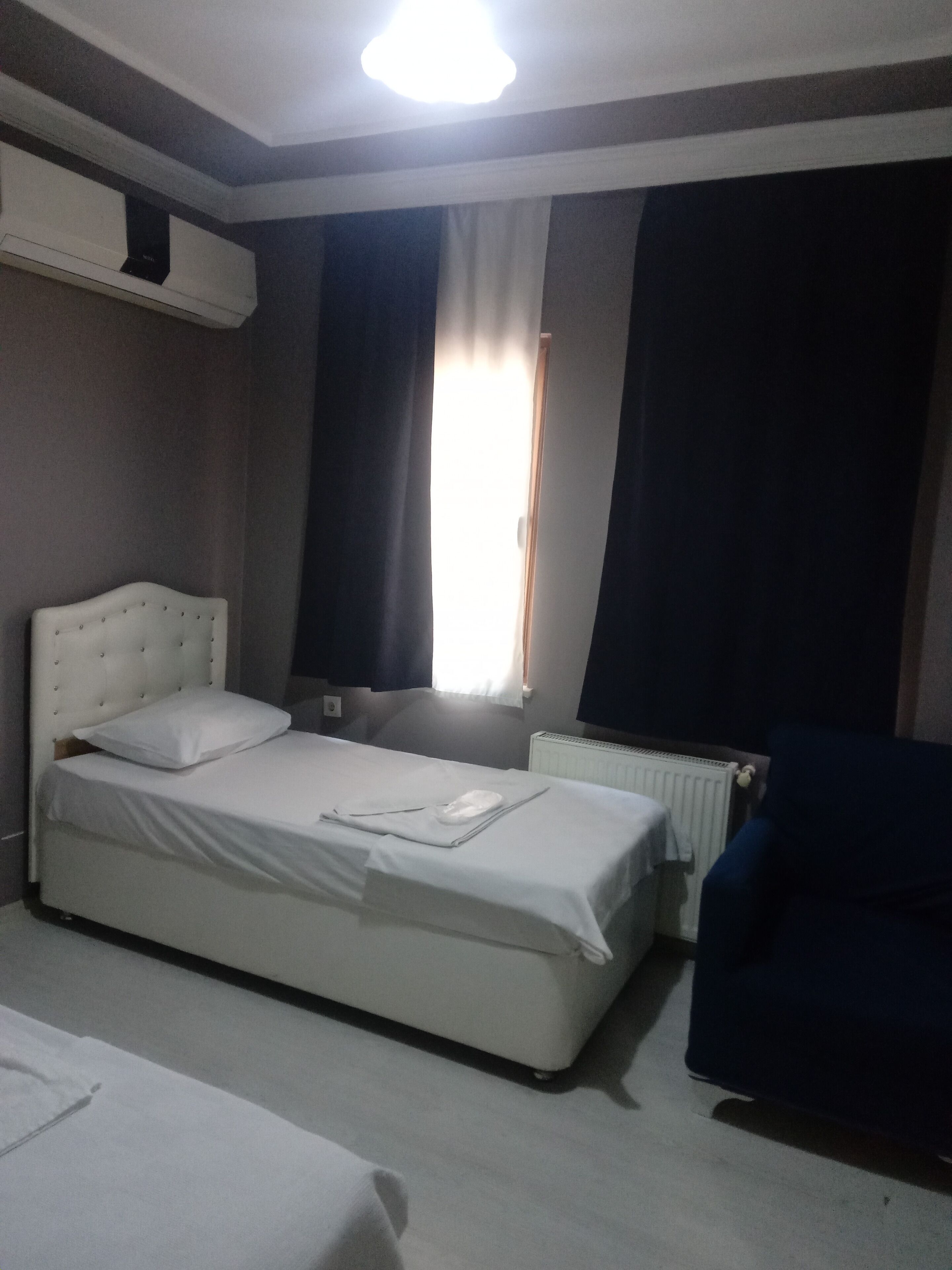 A bedroom with a single bed, a chair, a radiator, and a window with curtains.