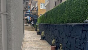 A narrow alleyway with a tiled floor, potted plants, a stone wall, and a green hedge. - Kalmuk Suite Hotel (Trabzon)