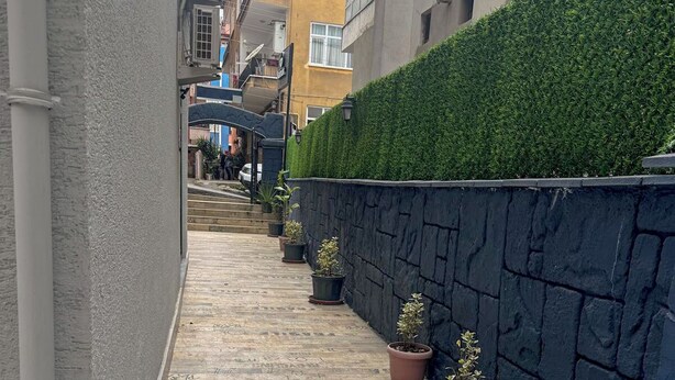 A narrow alleyway with a tiled floor, potted plants, a stone wall, and a green hedge. - Kalmuk Suite Hotel (Trabzon)